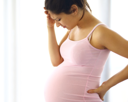 A pregnant woman with her hand to her head in stress.