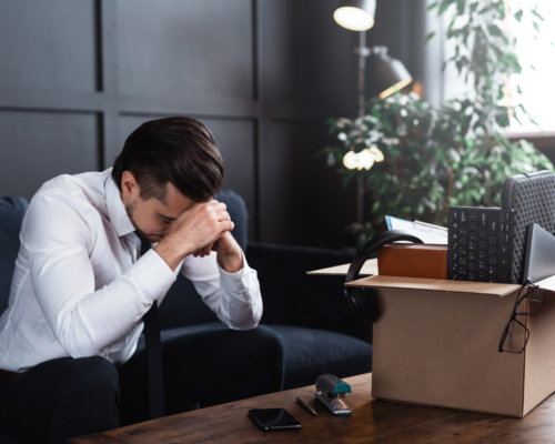 A man in business casual attire sitting in an office with a box of belongings.