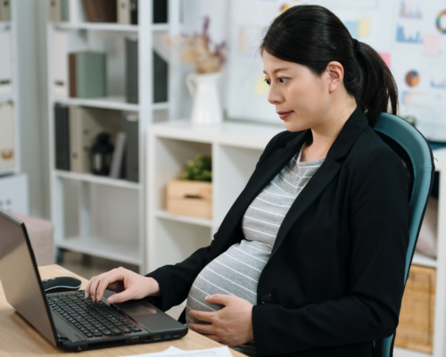A pregnant woman sitting at her work desk.